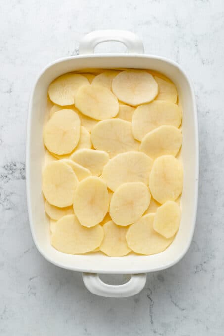 Overhead view of potato slices layered in baking dish