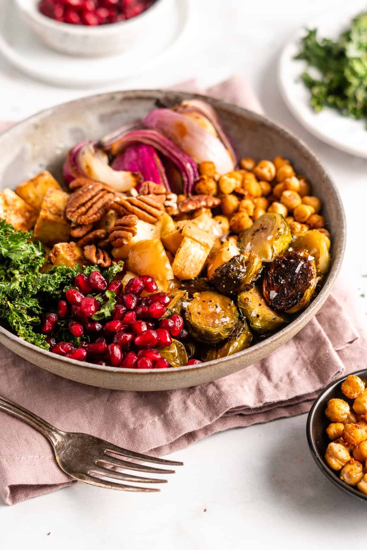 A Buddha bowl filled with pomegranate seeds, kale, Brussels sprouts, chickpeas, tofu, apples, and onions.