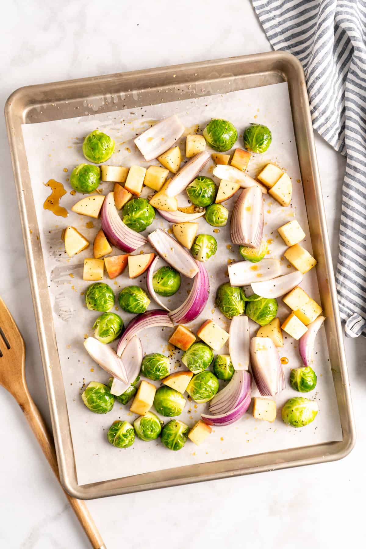 Overhead view of apples, Brussels sprouts, and red onions on parchment lined sheet pan