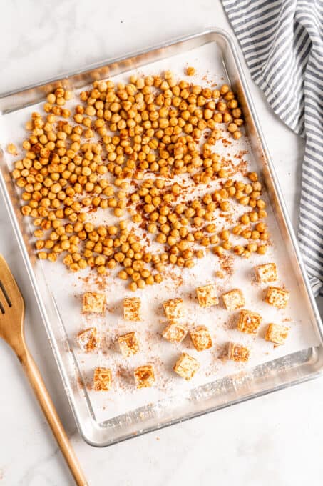 Overhead view of roasted chickpeas and tofu on a parchment lined sheet pan.