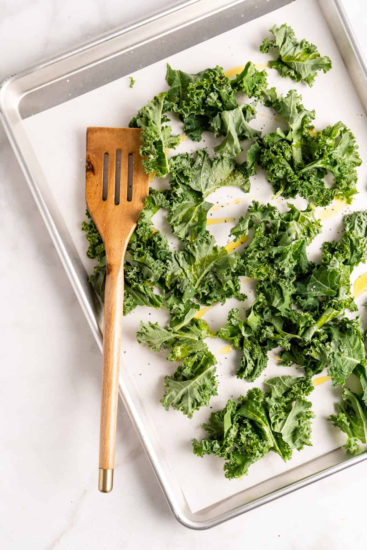 Overhead view of kale leaves on parchment-lined sheet pan with wooden spatula