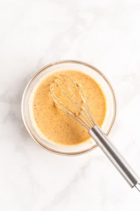 Overhead view of spicy tahini dressing in a glass bowl with a whisk.