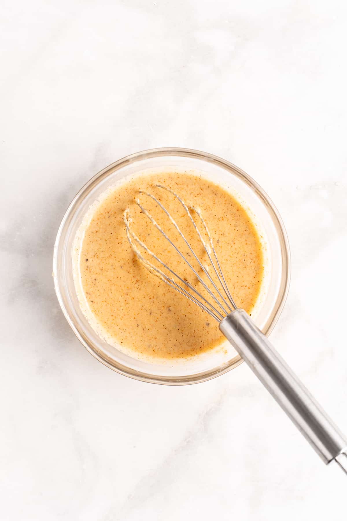 Overhead view of tahini dressing in glass bowl with whisk