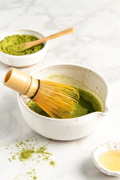 Make your own iced matcha latte at home! Matcha is a creamy, refreshing, caffeinated drink that's as delicious over ice as it is warm. Bamboo whisk in matcha bowl with brewed matcha