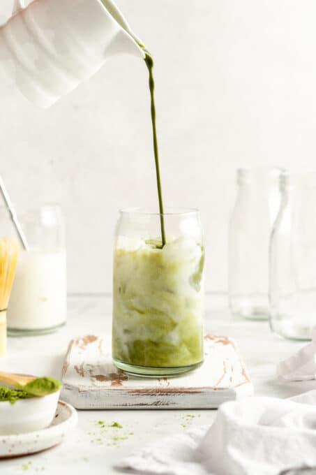 Pouring brewed matcha into glass tumbler filled with milk and ice