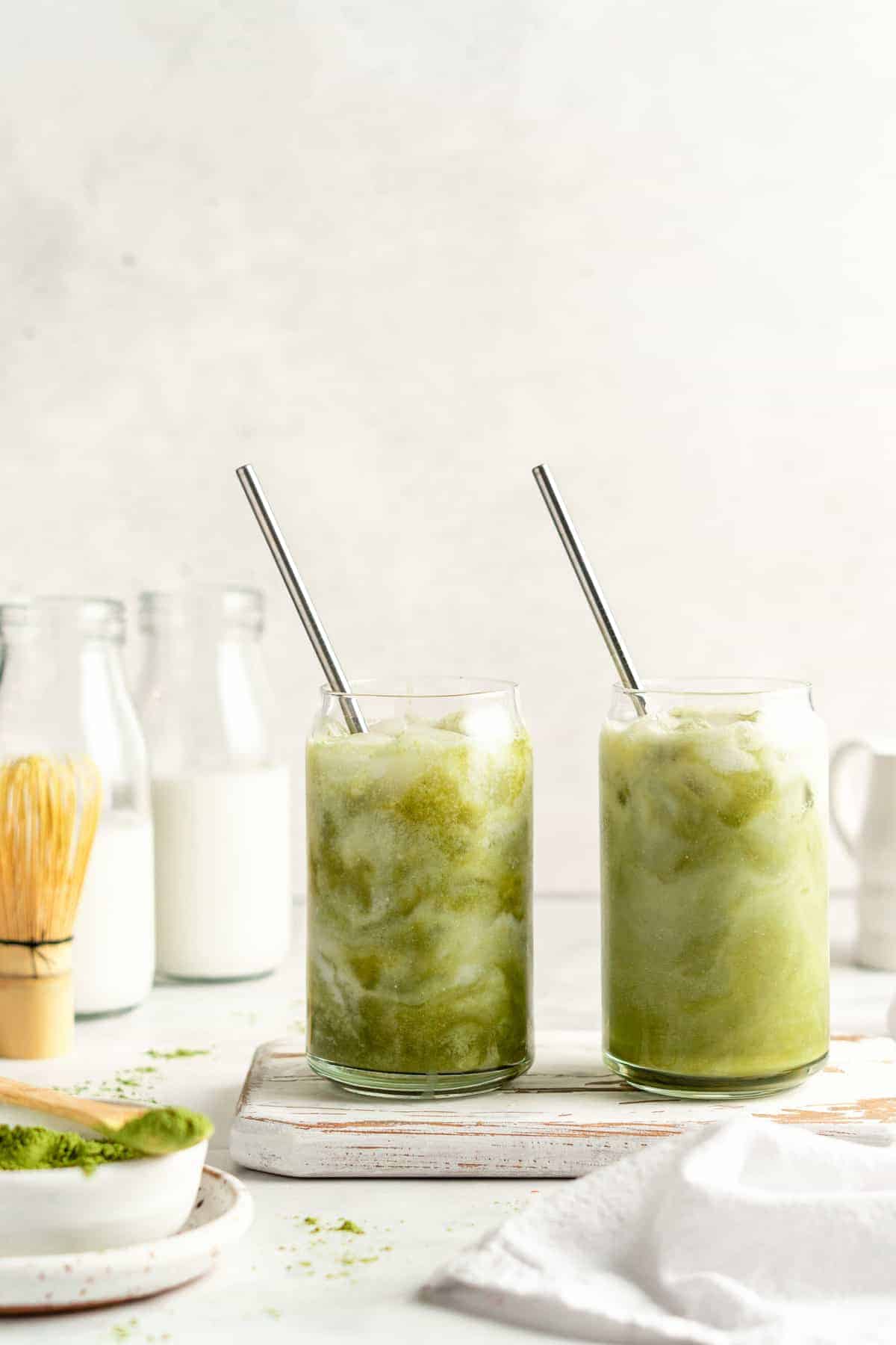 Two iced matcha lattes in glass tumblers with stainless steel straws; swirls of milk visible in glasses