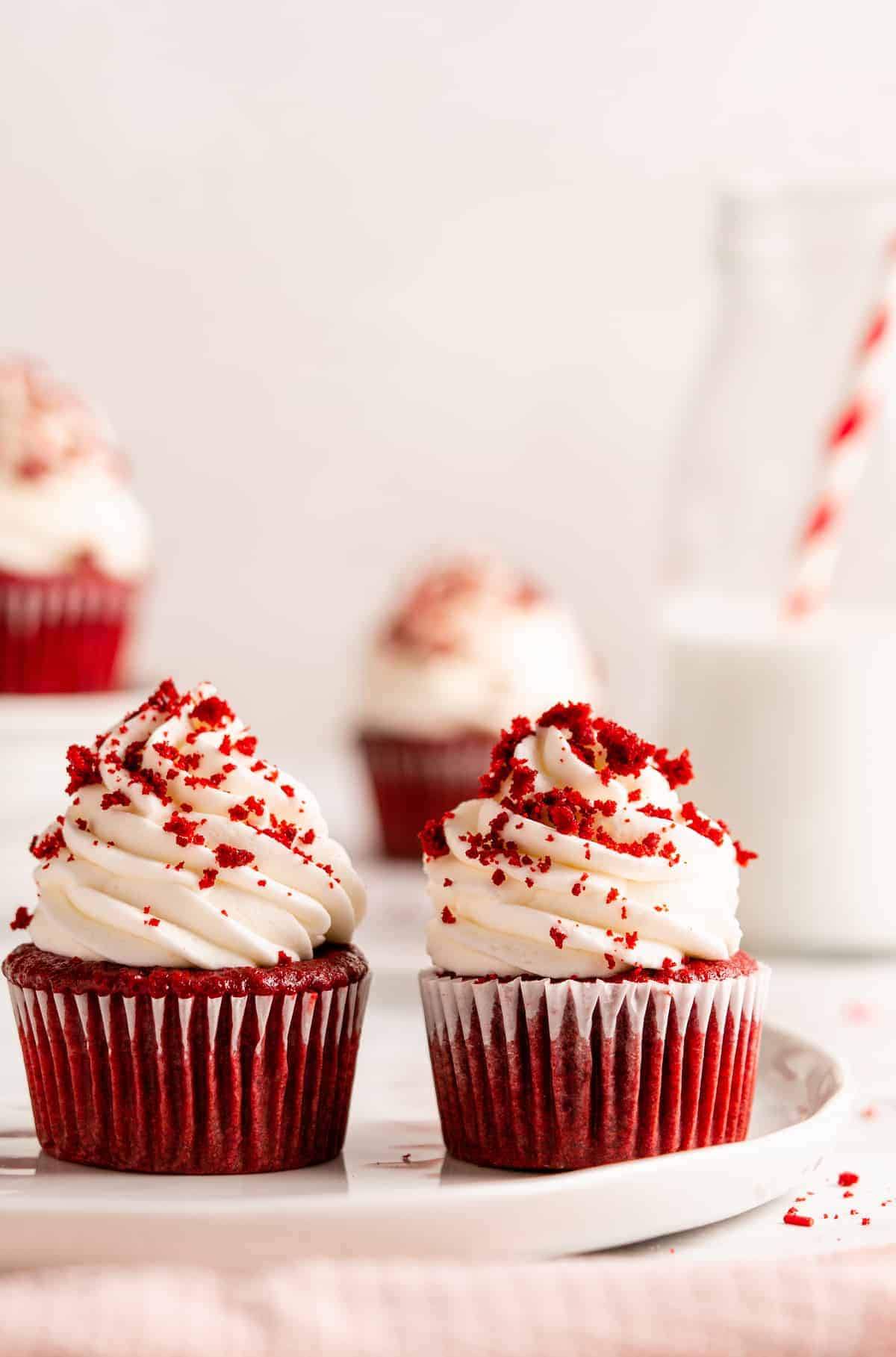Two red velvet cupcakes decorated with tall peaks of cream cheese frosting and cake crumbs