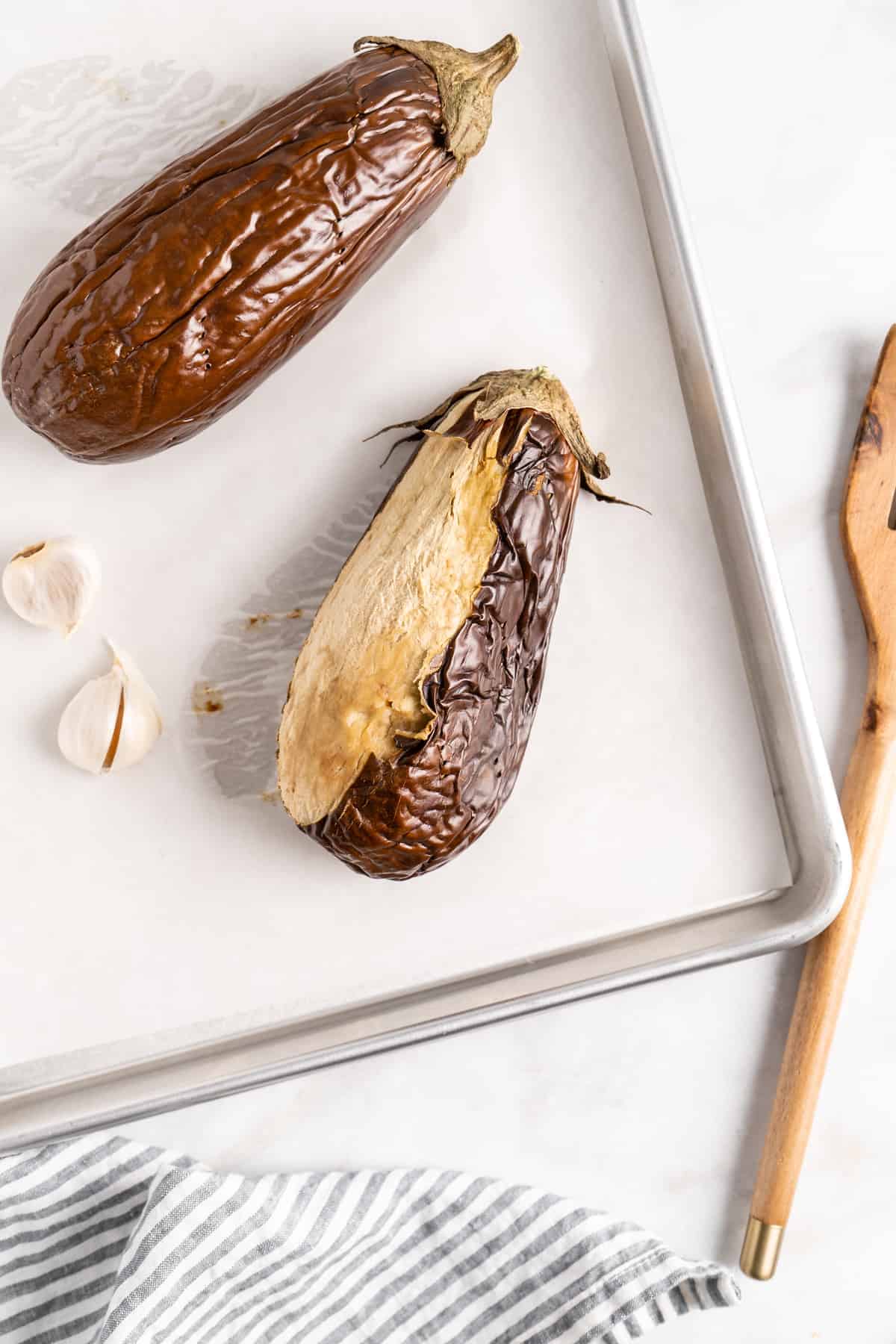 Roasted eggplants on baking sheet, with one half peeled