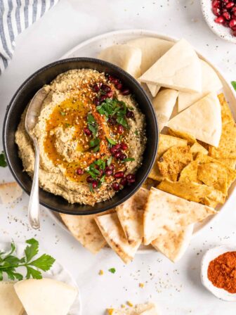 Overhead view of baba ghanoush in black bowl with spoon, surrounded by pitas on plate