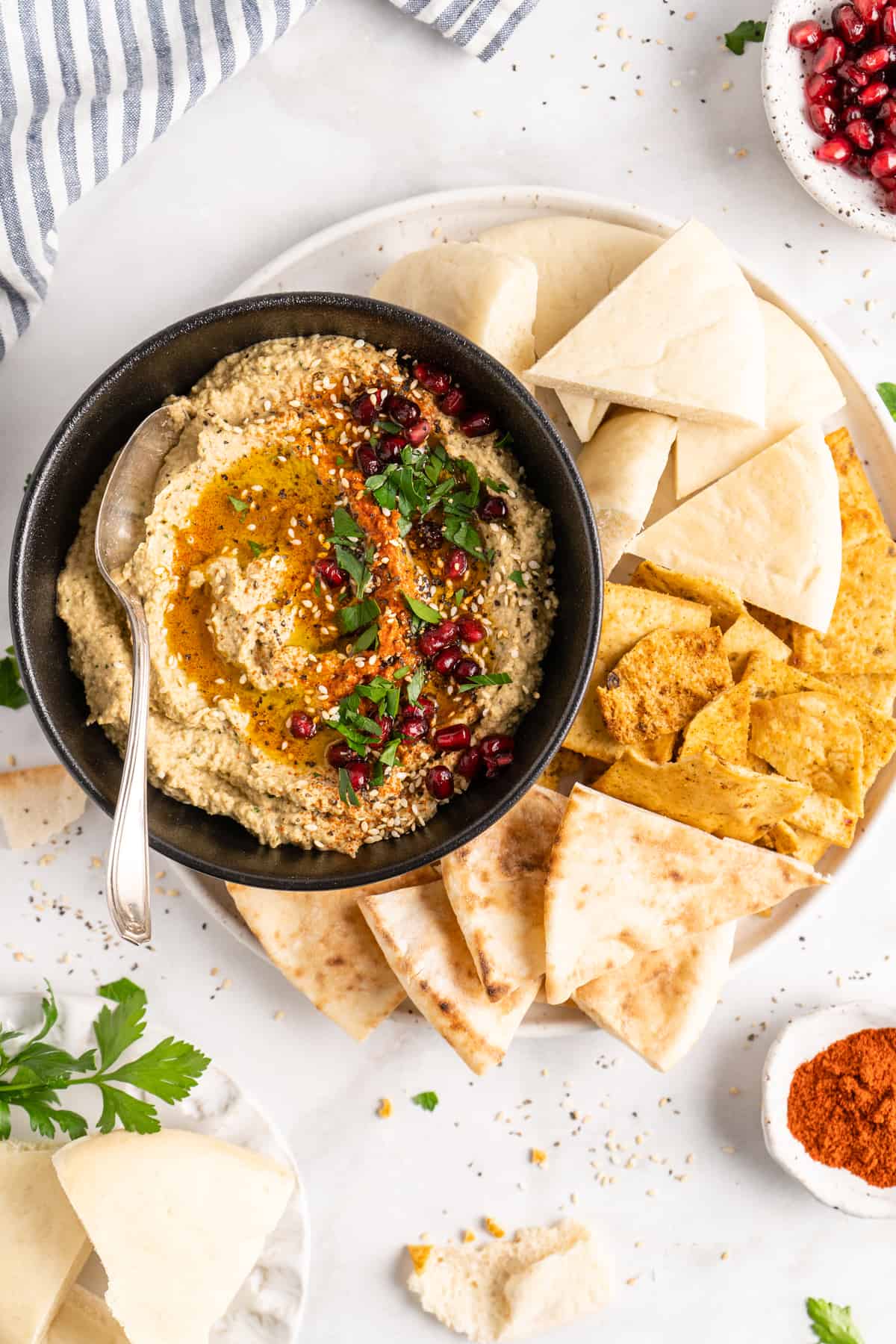 Overhead view of baba ghanoush in black bowl with spoon, surrounded by pitas on plate