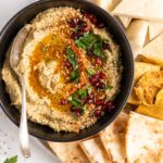 Overhead view of baba ghanoush in black bowl with spoon, surrounded by pitas