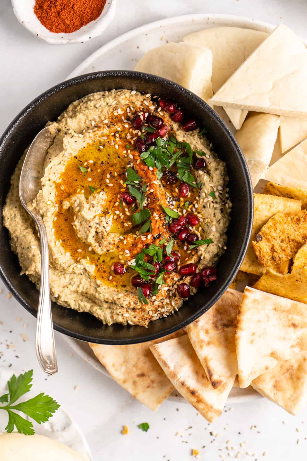 Overhead view of baba ghanoush in black bowl with spoon, surrounded by pitas