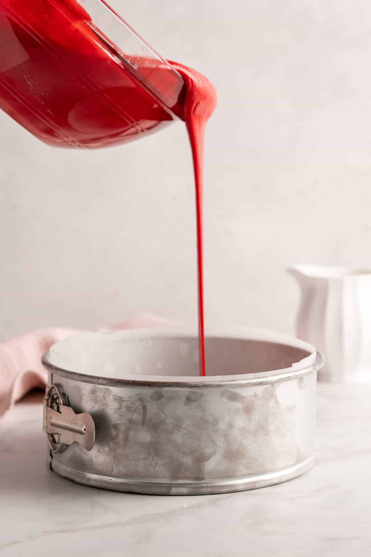 Pouring red velvet cake batter into lined cake pan