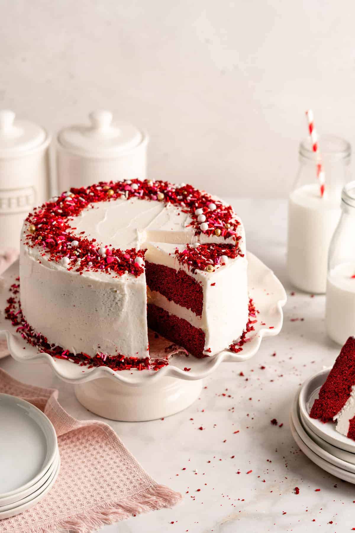 Vegan red velvet cake on cake stand with slice being removed