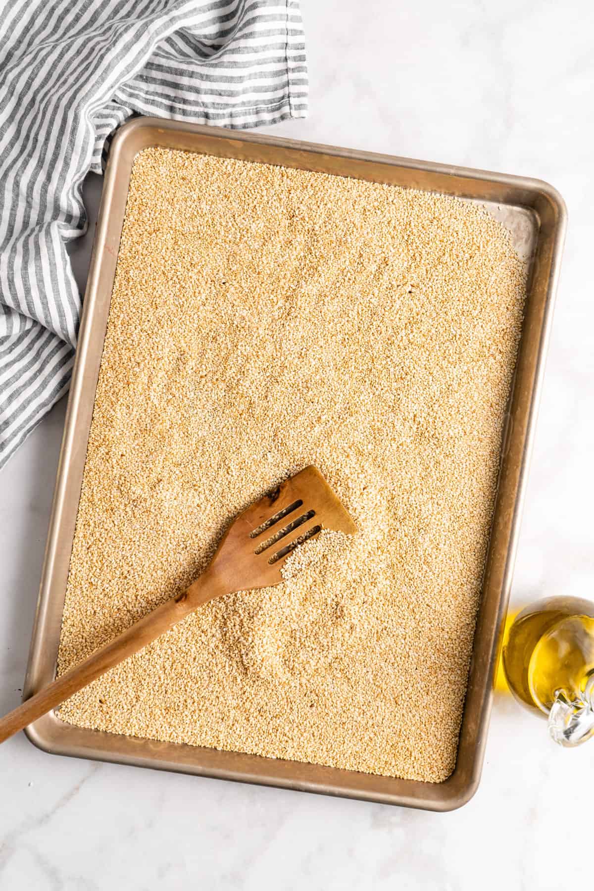 Overhead view of toasted sesame seeds on sheet pan with wooden spatula