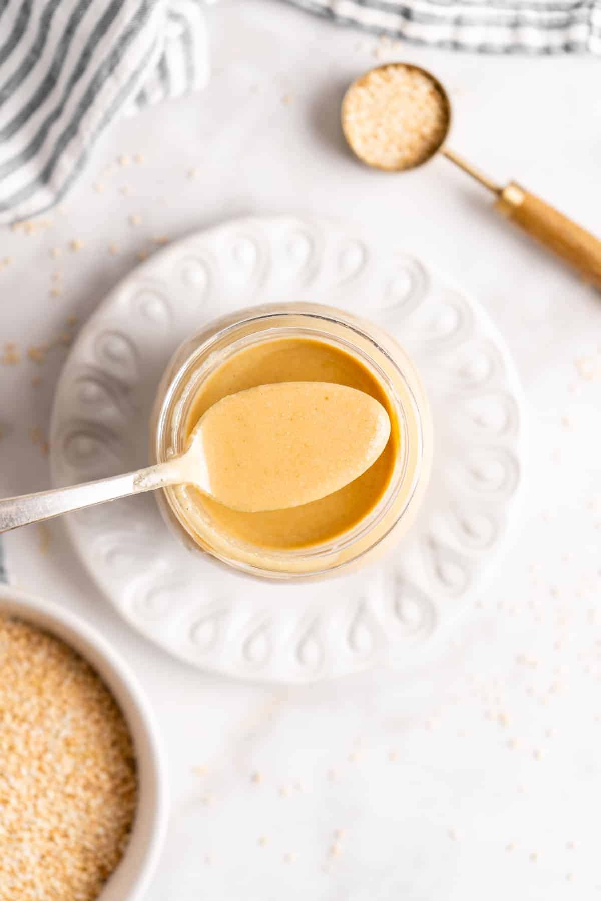 Overhead view of spoonful of tahini being held over jar