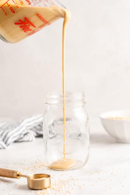 Measuring cup of tahini being poured into jar