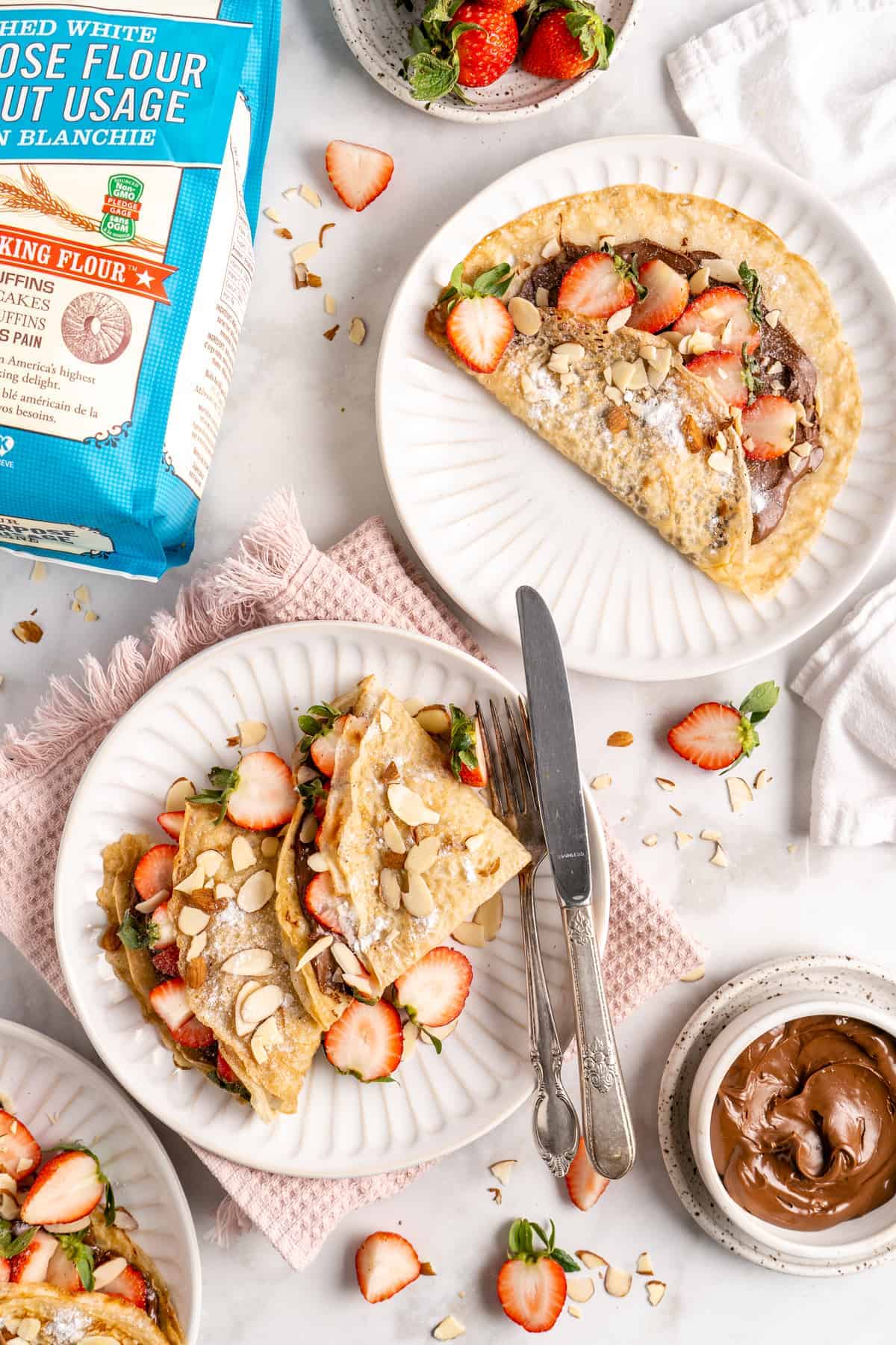 Overhead view of vegan crepes on plates with strawberries and hazelnut spread