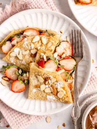 crepes on a plate with a fork with strawberries and nuts on top