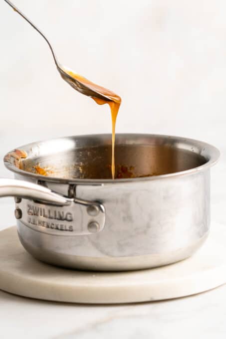 Sticky orange sauce dripping from spoon into saucepan