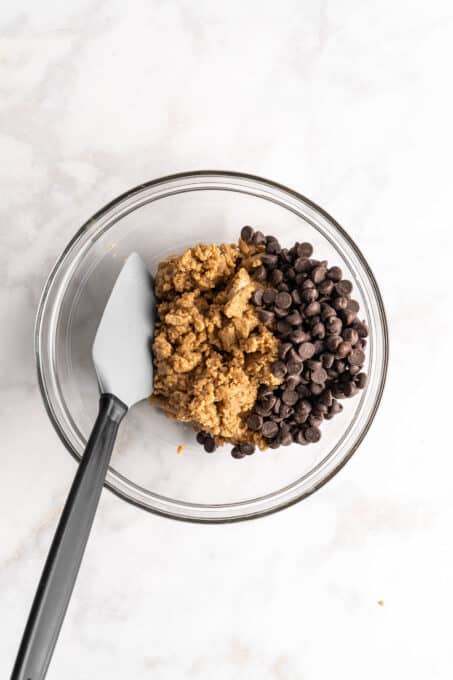 Overhead view of cookie dough and chocolate chips in glass bowl with spatula