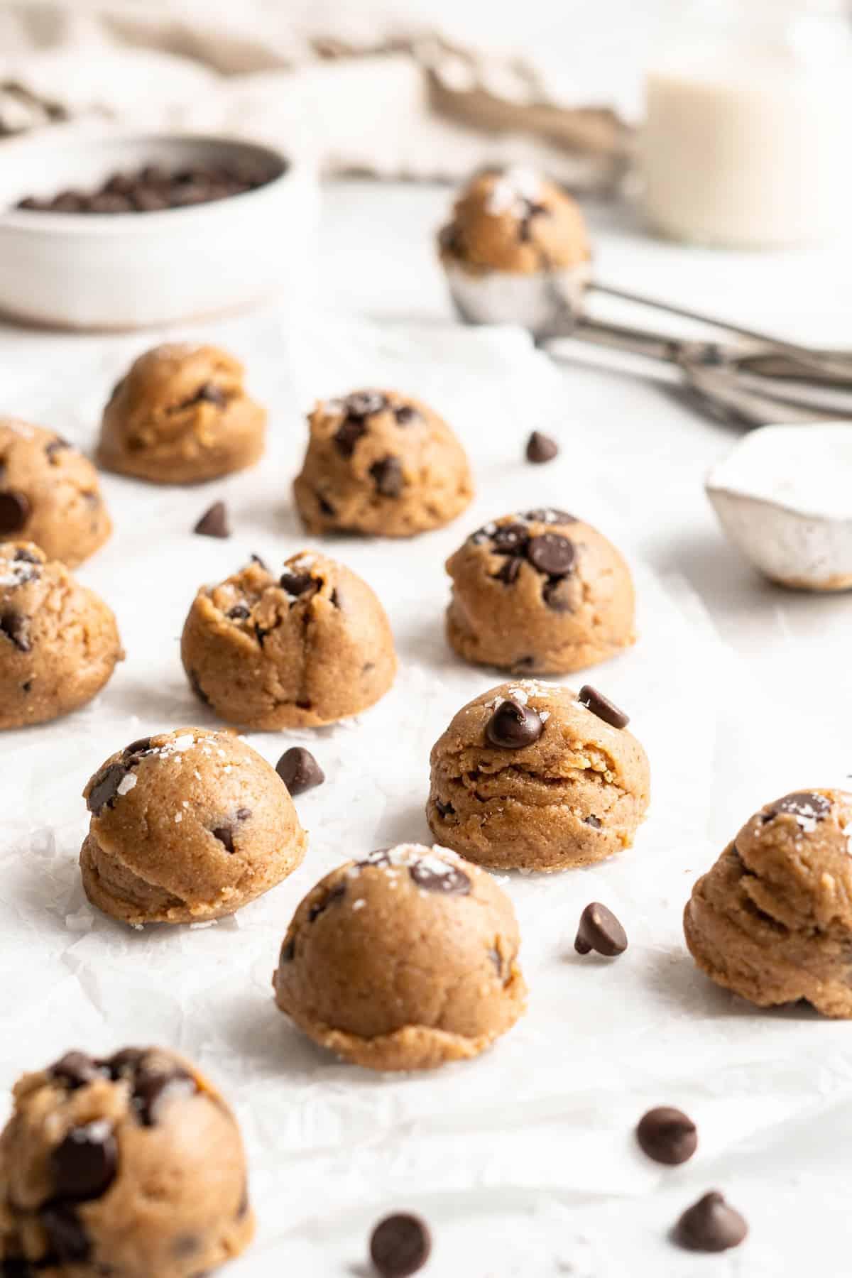 Vegan cookie dough balls on parchment paper with chocolate chips scattered between