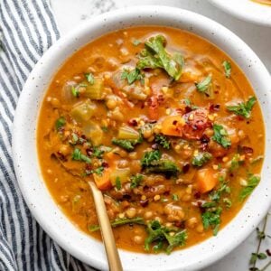 Overhead view of chunky lentil soup in white bowl with gold spoon