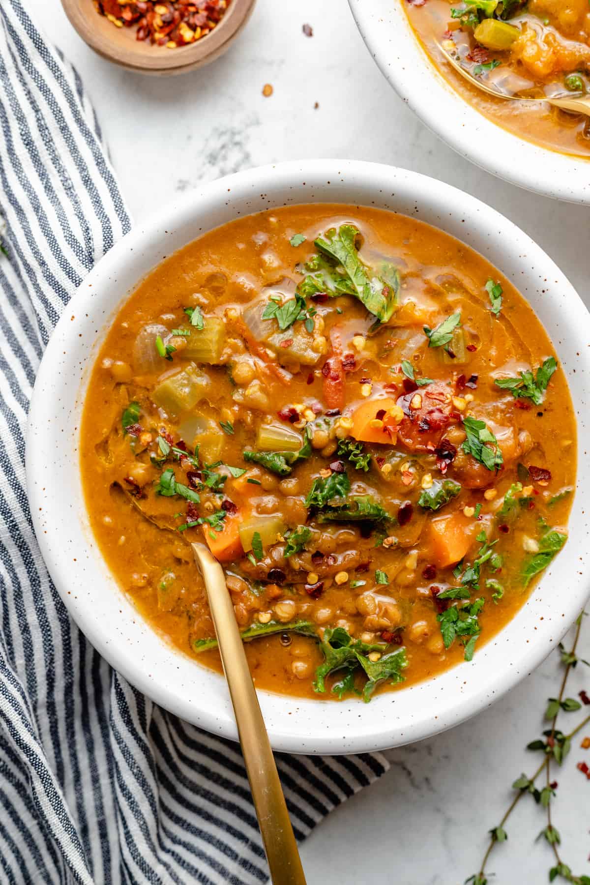 Overhead view of chunky lentil soup in white bowl with gold spoon