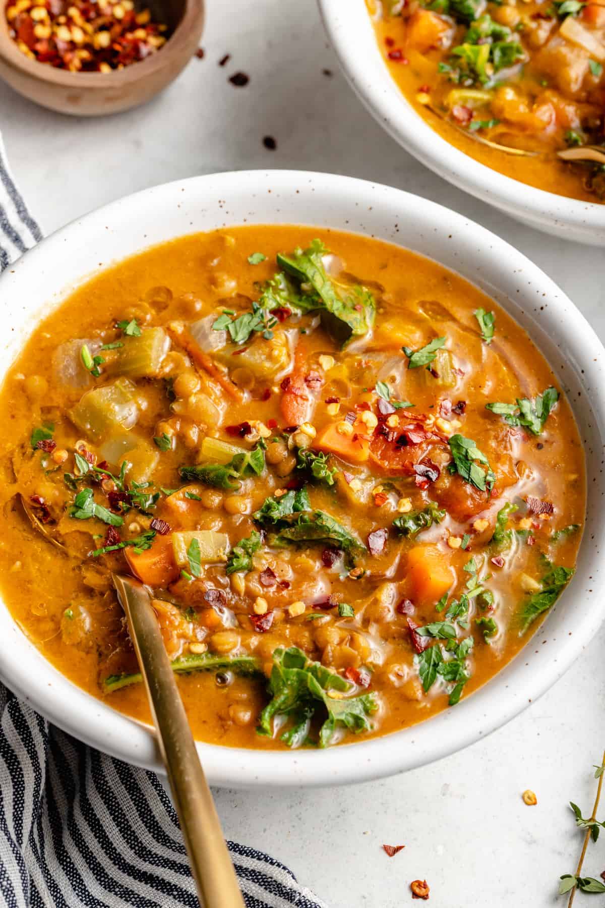 Chunky lentil soup in white bowl with gold spoon