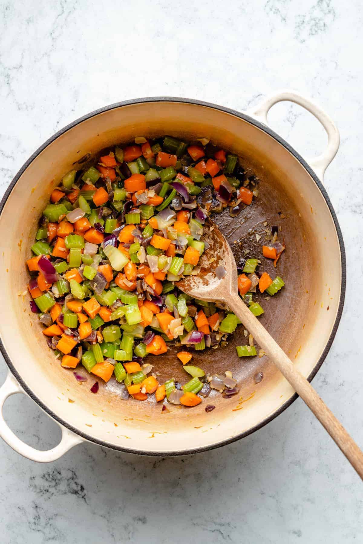 Overhead view of celery, carrots, and onions in large pot with wooden spoon