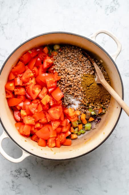 Overhead view of lentil soup ingredients in pot with wooden spoon
