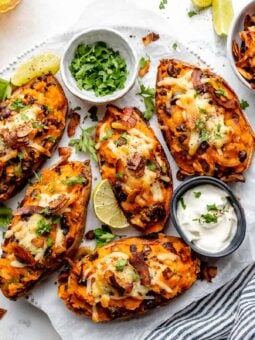Overhead view of loaded sweet potato skins on plate with bowls of yogurt and cilantro