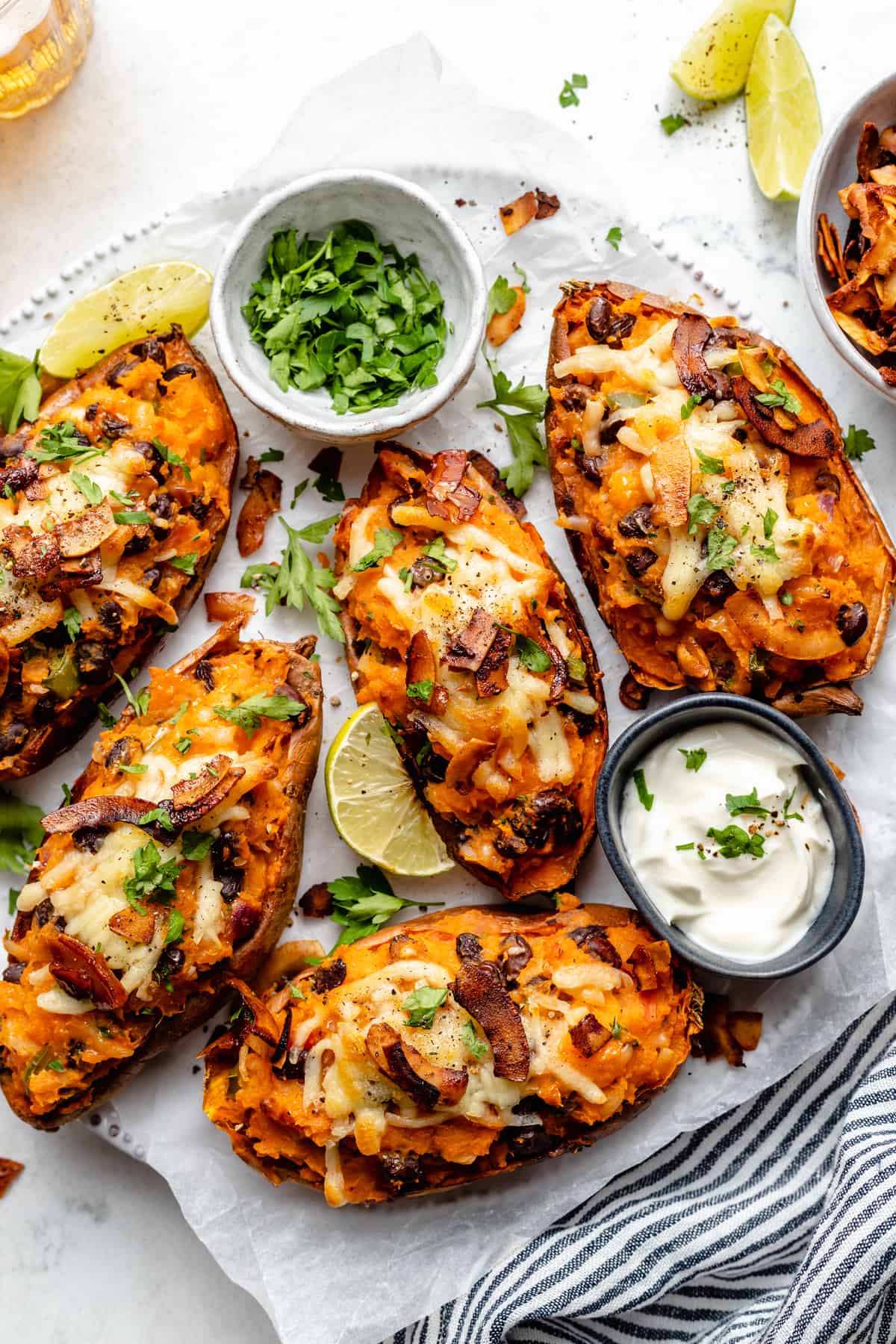Overhead view of loaded sweet potato skins on plate with bowls of yogurt and cilantro