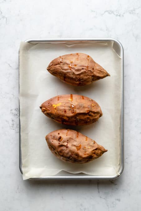 Overhead view of 3 baked sweet potatoes on parchment lined baking sheet
