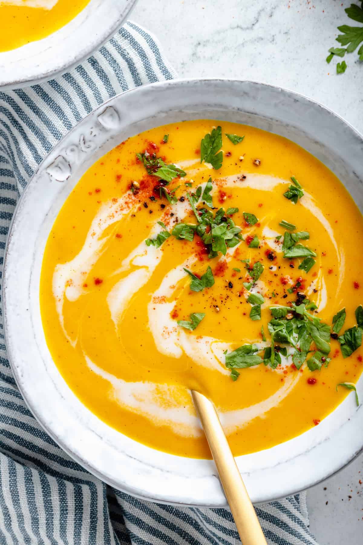 Overhead view of roasted carrot soup in bowl, swirled with coconut milk and garnished with cilantro and cayenne