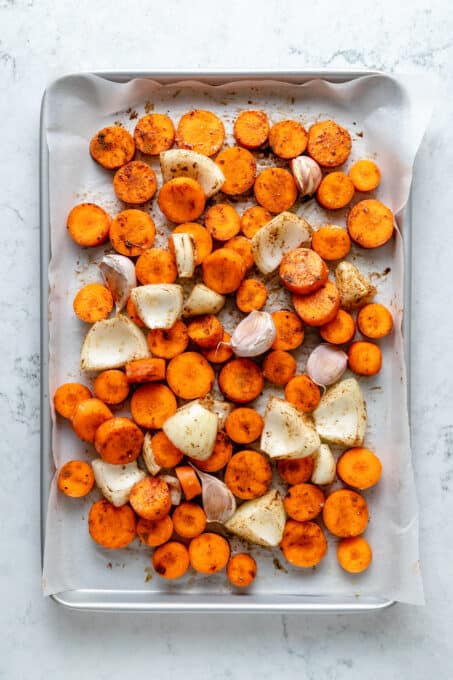Overhead view of carrots, onions, and garlic on parchment-lined sheet pan
