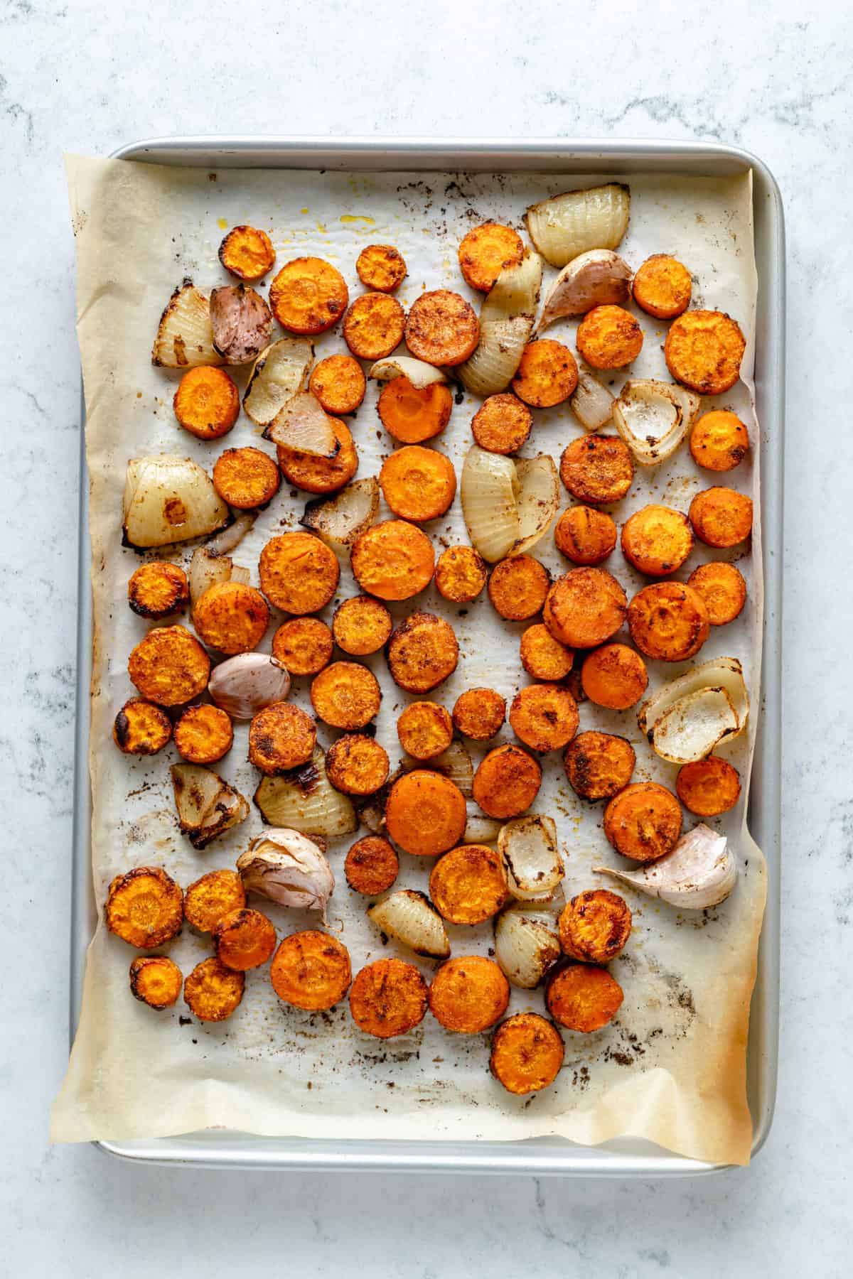 Overhead view of roasted carrots, onions, and garlic on sheet pan