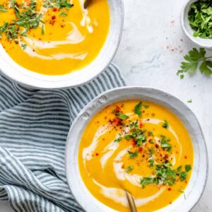 Two bowls of roasted carrot soup on blue and white striped tea towel