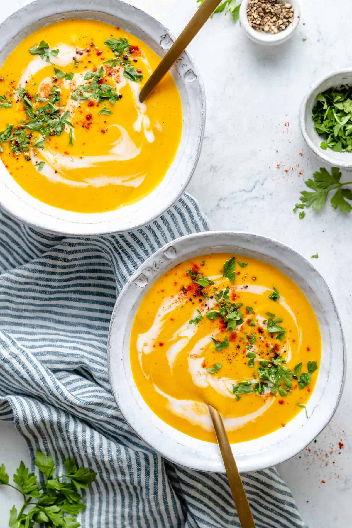Two bowls of roasted carrot soup on blue and white striped tea towel