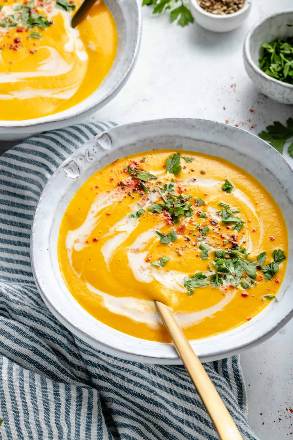 Carrot soup in bowl with spoon set on striped tea towel