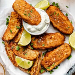 Overhead view of vegan fish sticks on parchment lined plate with one stick being dipped in sauce