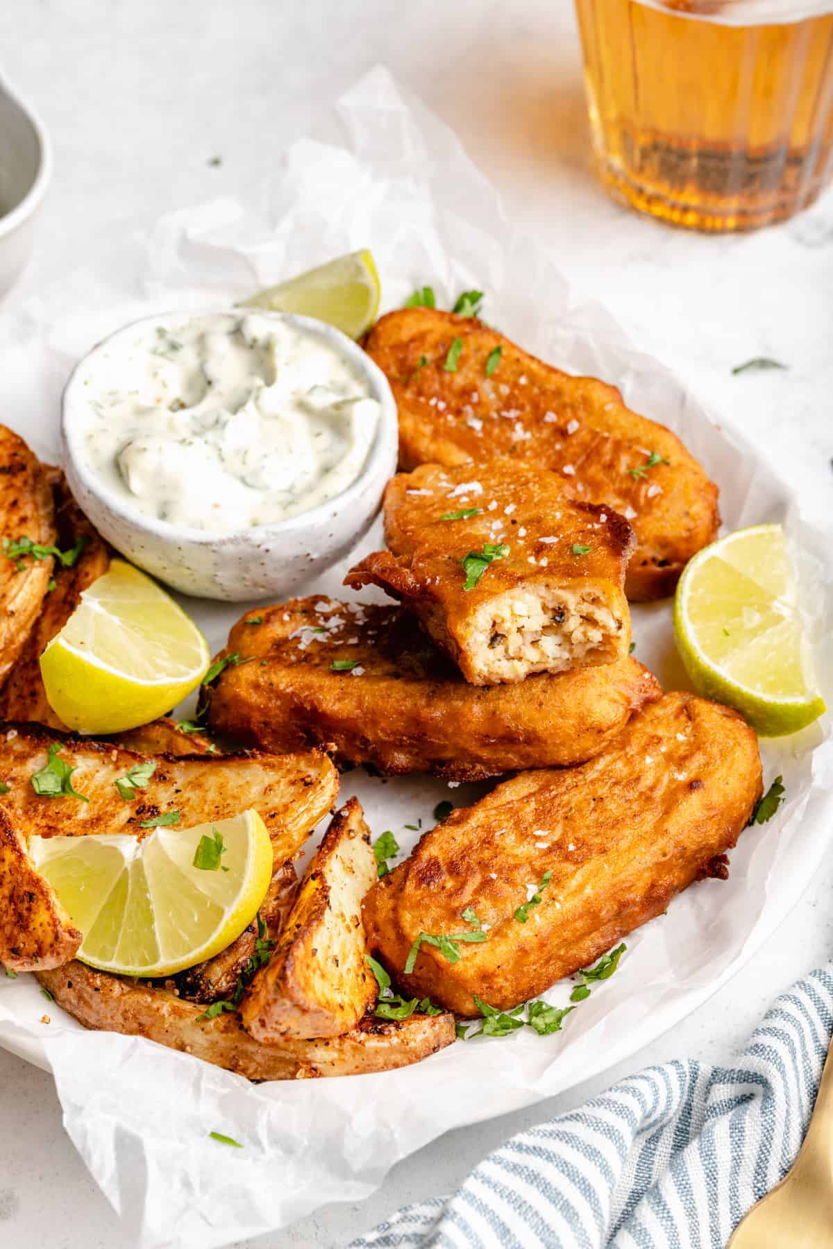 Vegan fish sticks on parchment-lined plate with lime wedges and bowl of tartar sauce
