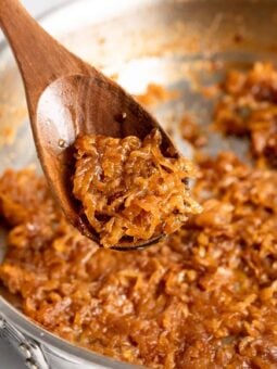 Closeup of caramelized onions on wooden spoon with skillet in background