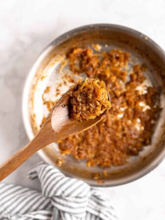 Caramelized onions on wooden spoon above pan