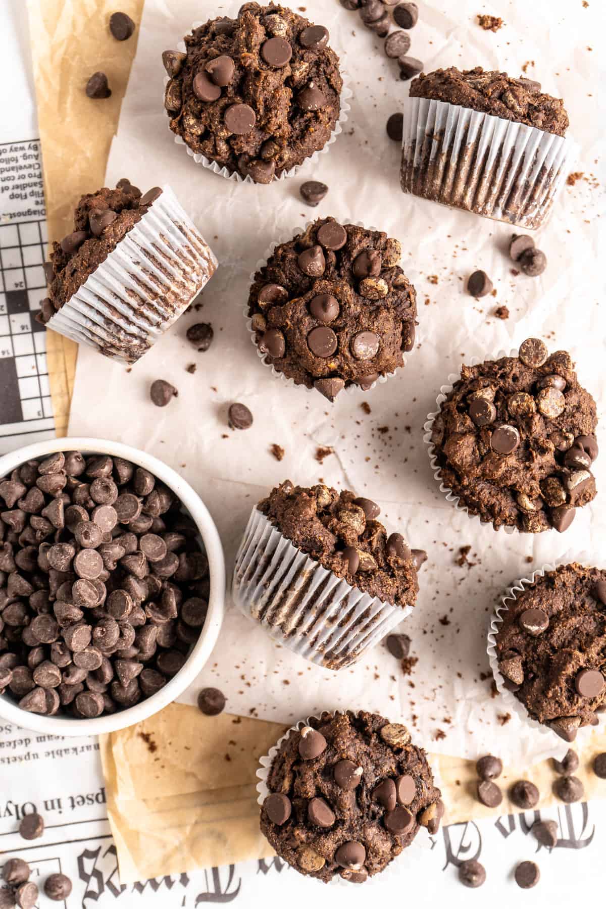Double Chocolate Banana Muffins on parchment paper set over newspaper with bowl of chocolate chips