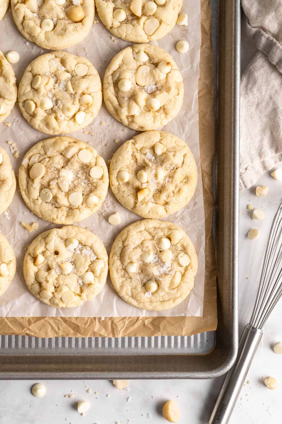 White Chocolate Macadamia Nut Cookies on parchment lined baking sheet set next to whisk