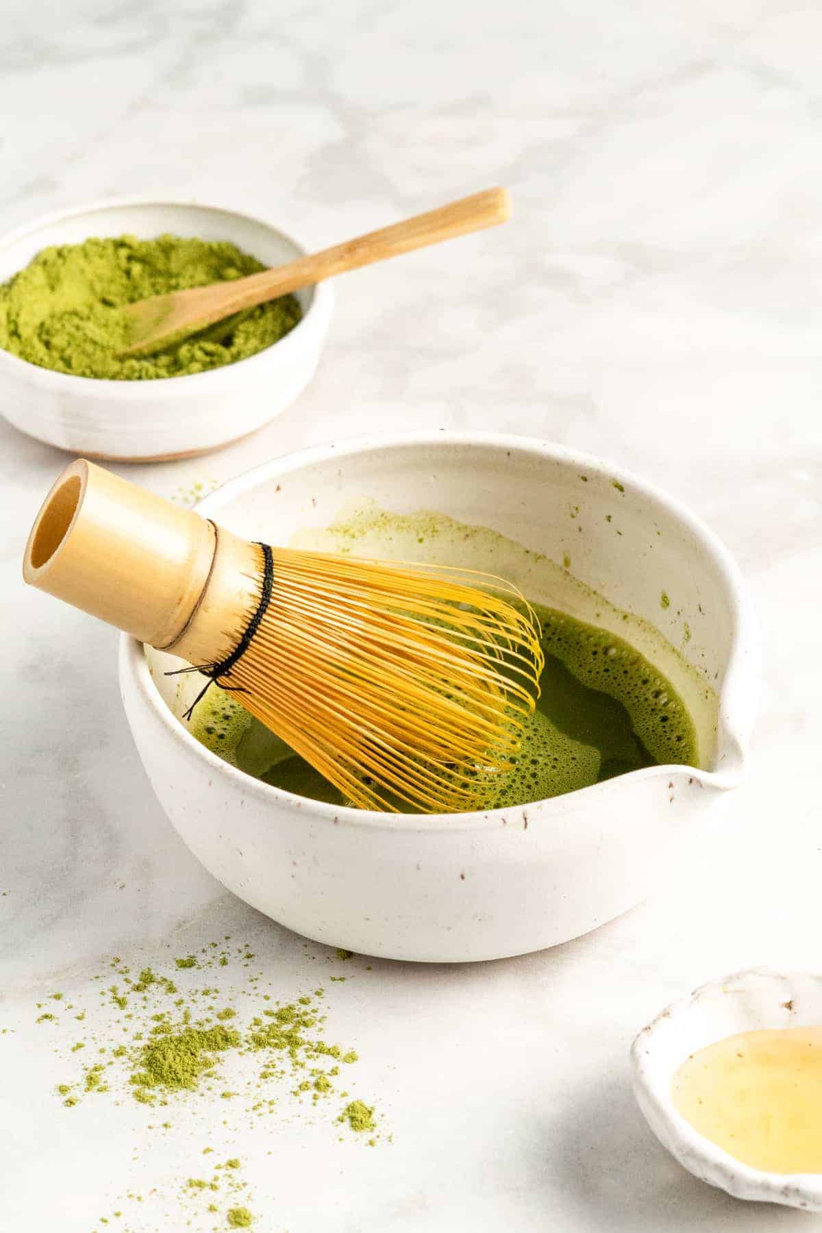 Bamboo matcha whisk in white bowl with matcha and water