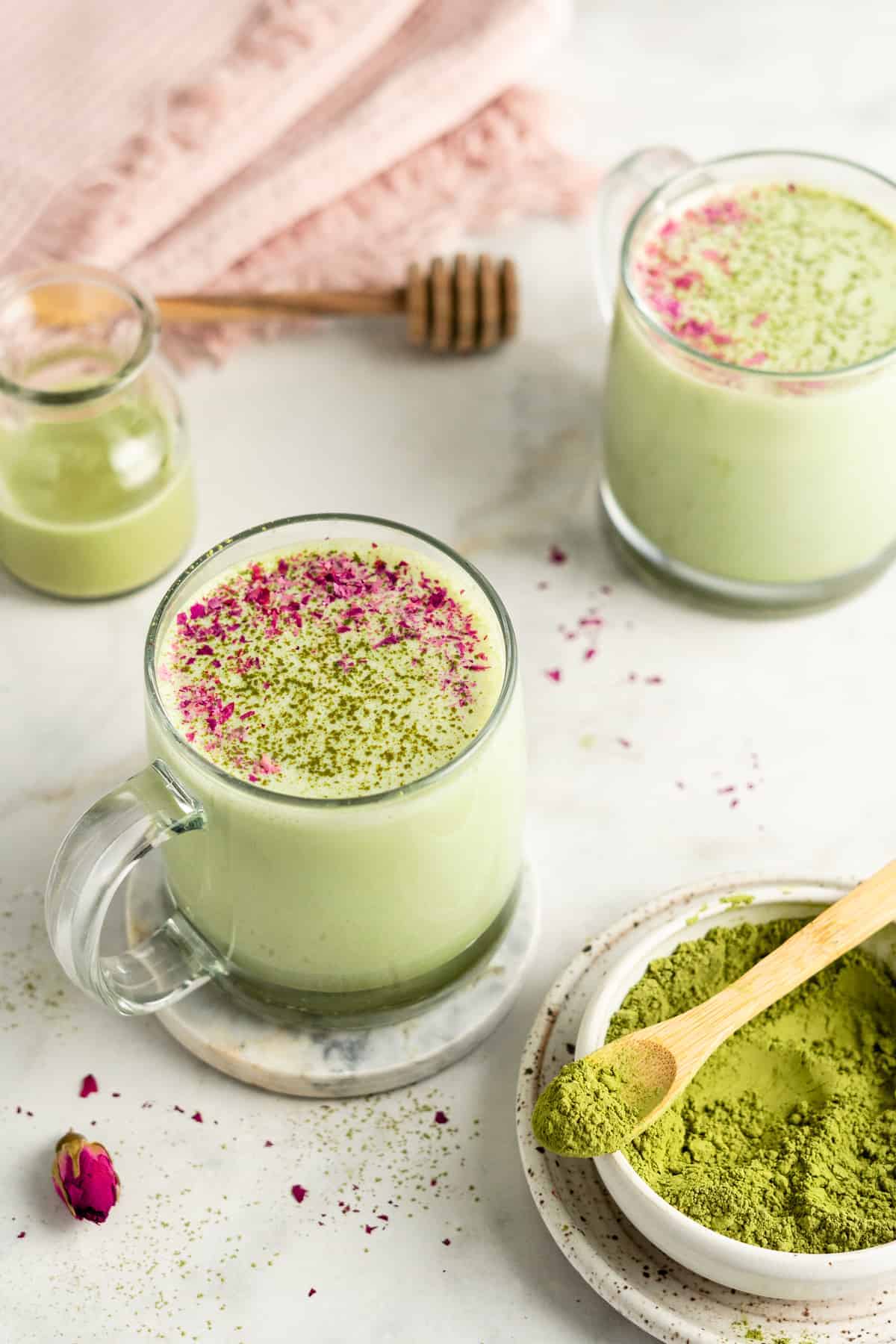 Matcha latte in two glass mugs with bowl of matcha in foreground