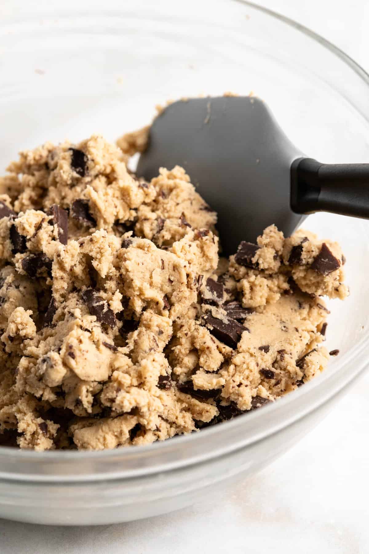 Chocolate chip cookie dough in glass bowl with rubber spatula