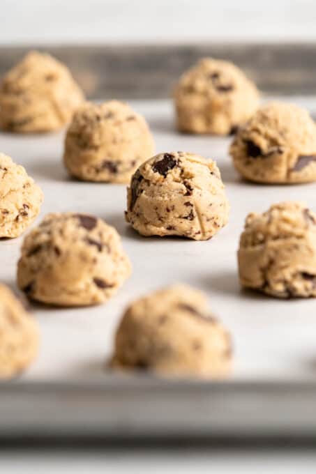 Balls of chocolate chip cookie dough on parchment lined baking sheet